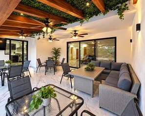 A modern living room with a glass table, seating area, ceiling fans, and a view through large windows. - Private Boutique Hotel Buyout & Luxury (Puerto Vallarta)