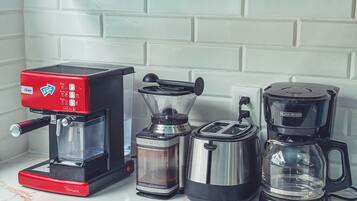 Una cocina con cafetera, licuadora, tostadora y jarra de café sobre la encimera.