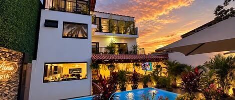 Un edificio moderno de dos pisos con piscina, asientos al aire libre y vista al atardecer.