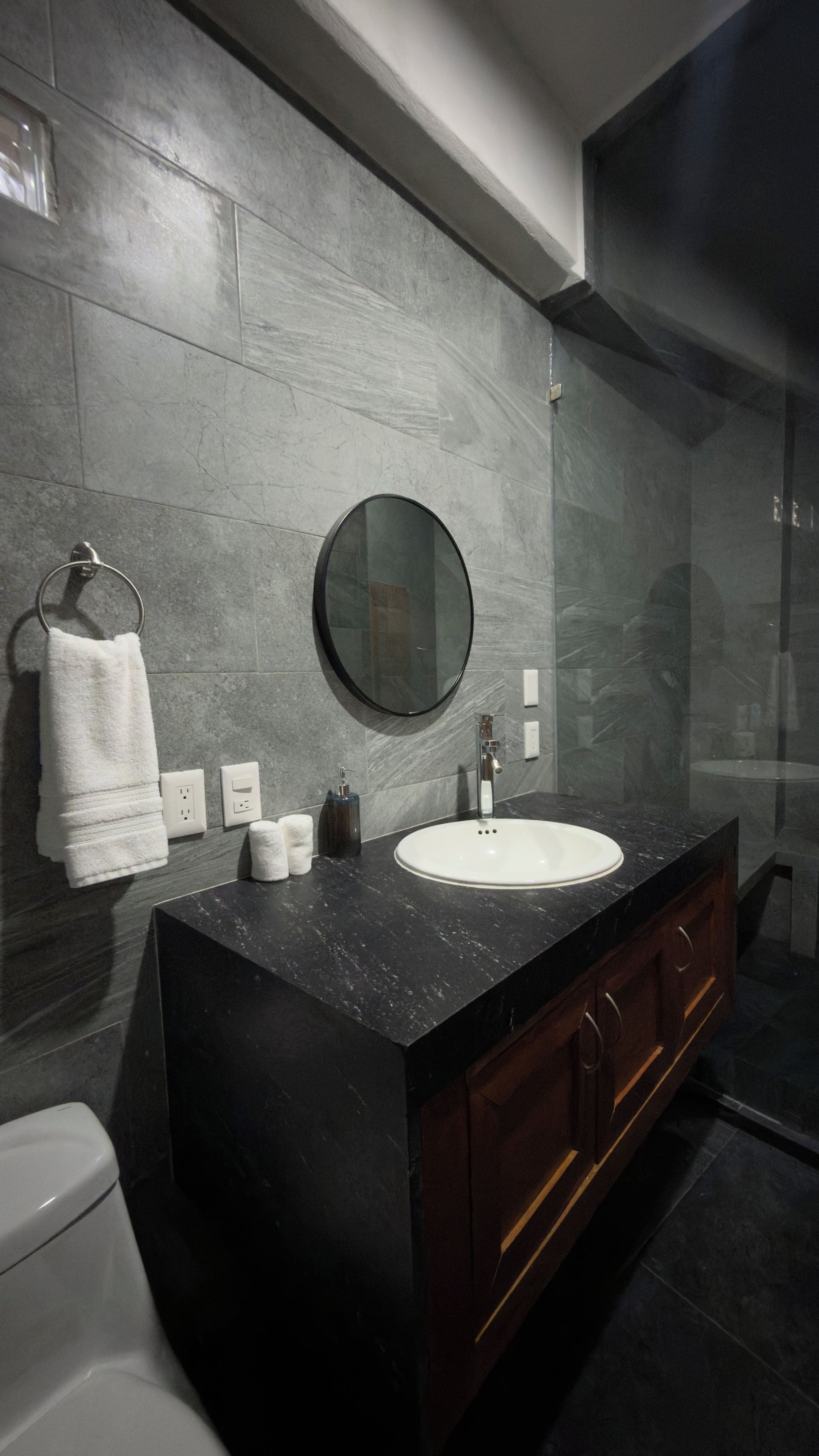 A modern bathroom with a black marble vanity, a round mirror, and a white sink.