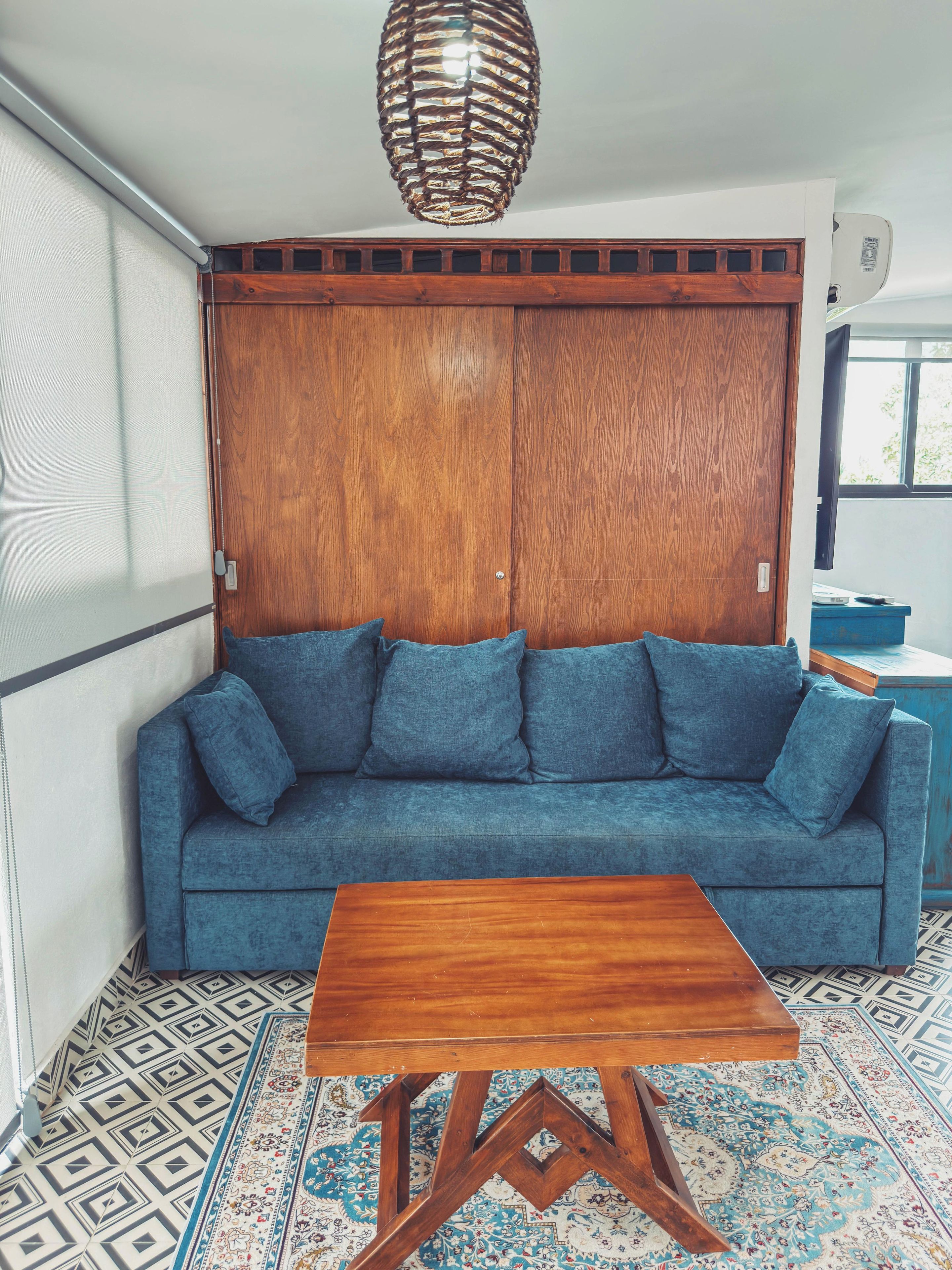 A room with a blue sofa, a wooden table, patterned floor, and a hanging light fixture.