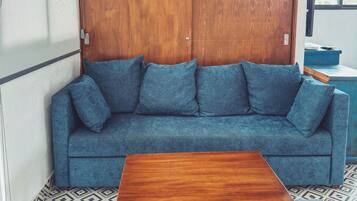 A room with a blue sofa, a wooden table, patterned floor, and a hanging light fixture.