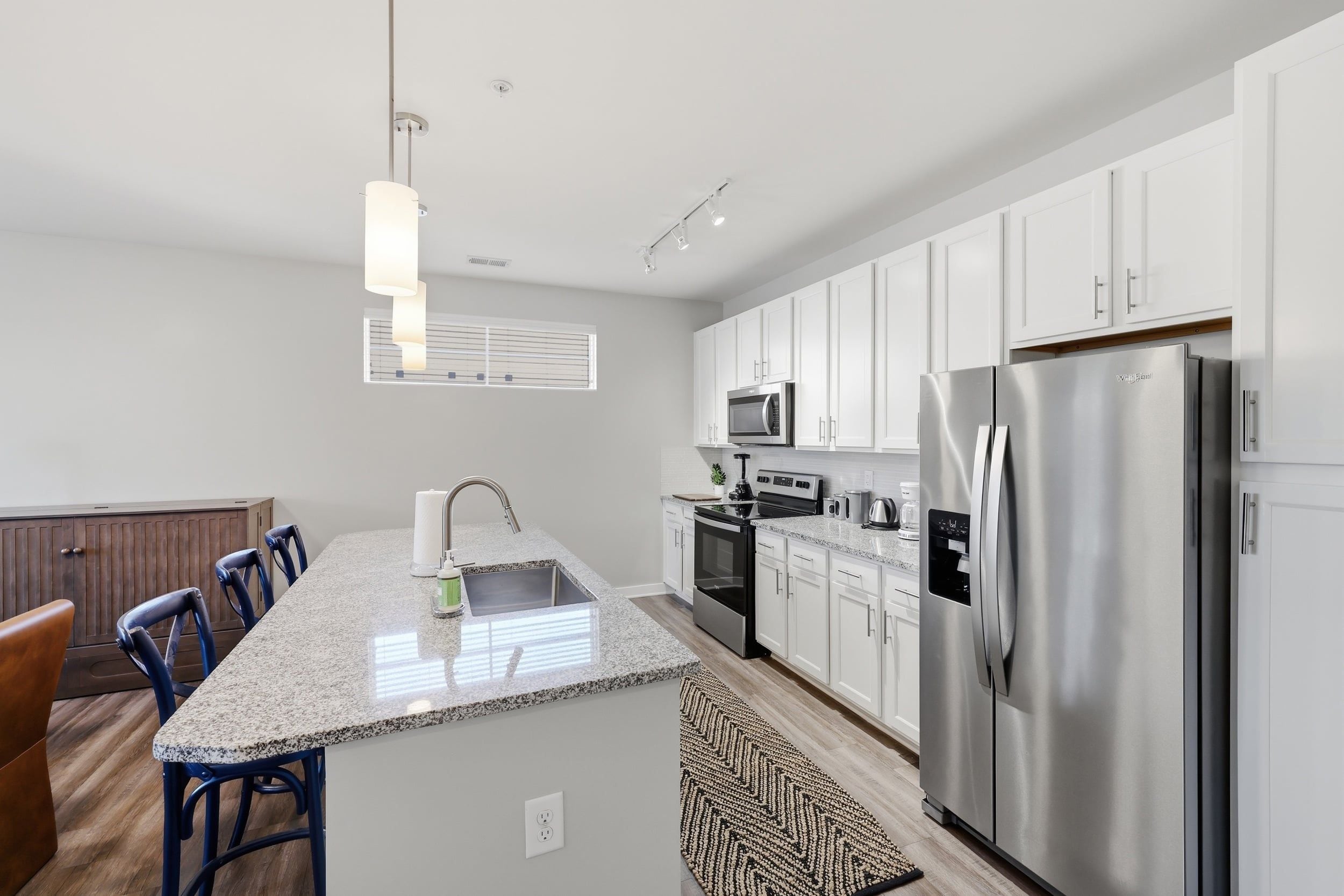 Cozinha moderna com armários brancos, eletrodomésticos de aço inoxidável, bancada de granito e ilha integrada com assentos.