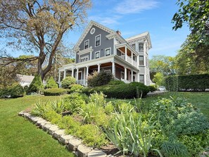 A two-story house with a front porch, surrounded by a well-maintained garden with various plants and a lawn.