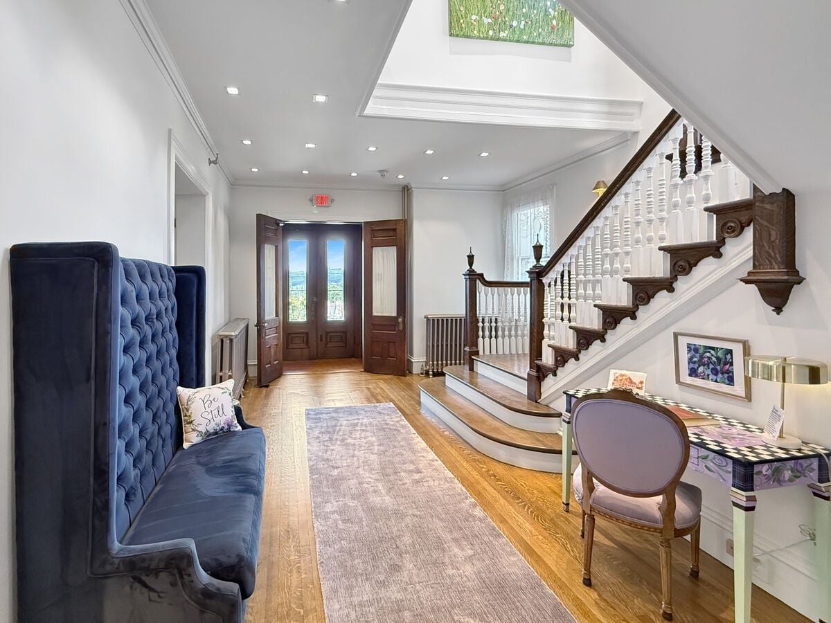 A spacious hallway with a blue upholstered bench, a wooden staircase, and a table with a chair.