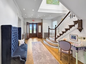 A spacious hallway with a blue upholstered bench, a wooden staircase, and a table with a chair.
