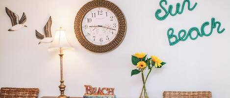 Una habitación con un reloj de pared, una lámpara, un jarrón con flores y un letrero que dice 'BEACH'.