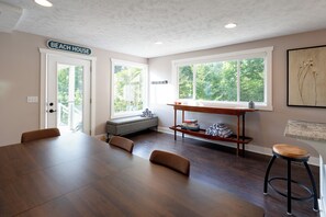A spacious room with a large dining table, a bench, and a window with a view of trees. - Beautiful Day | Large Grand Haven Retreat with Spectacular Lake Michigan Views + Beach (Grand Haven)