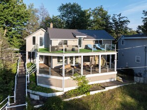 Ein zweigeschossiges Haus mit einer verglasten Terrasse und einer kleinen Sitzgelegenheit im Freien.