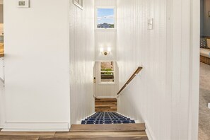 A staircase with a wooden handrail leading to a landing with a door and windows. - Half Moon Haven Ocean-view, hot tub, pool, and beach access. (Duck)
