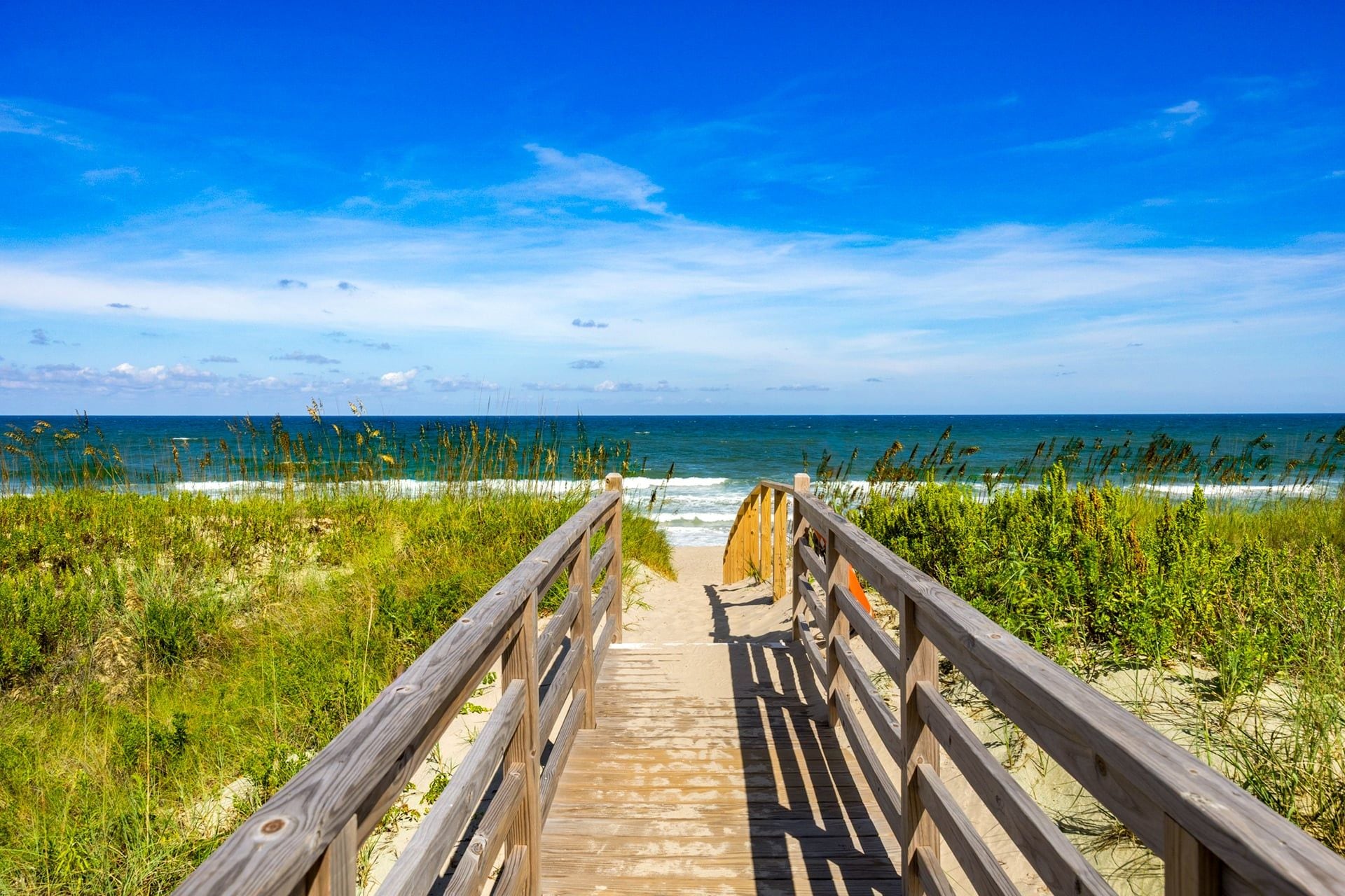 A wooden boardwalk leading to a beach with a clear view of the ocean.