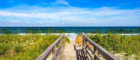 A wooden boardwalk leading to a beach with a clear view of the ocean.