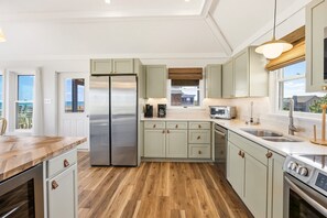 A modern kitchen with a stainless steel refrigerator, wooden flooring, and light-colored cabinets. - Half Moon Haven Ocean-view, hot tub, pool, and beach access. (Duck)