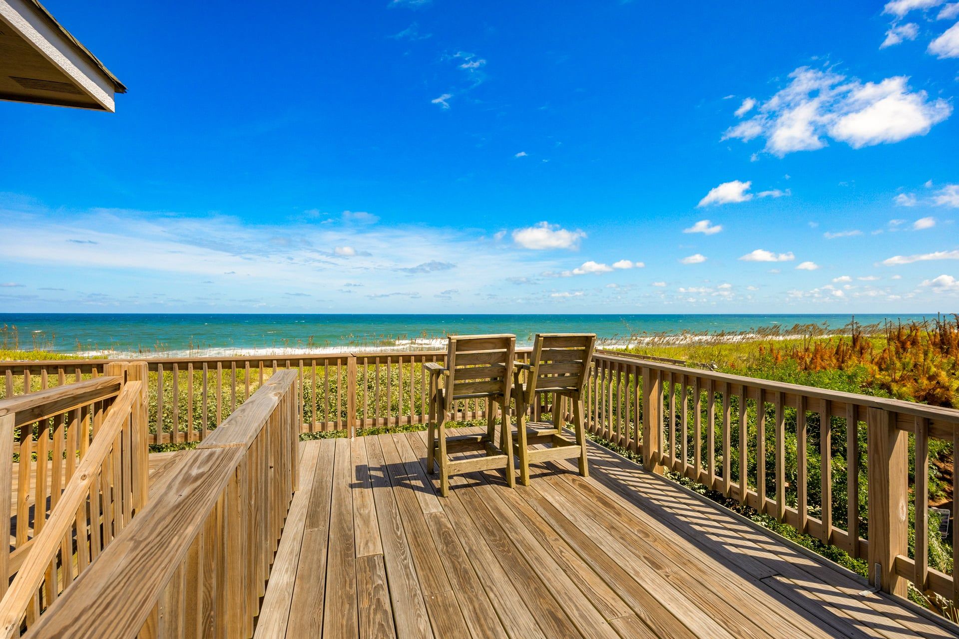 A wooden deck with two chairs overlooking a beach.