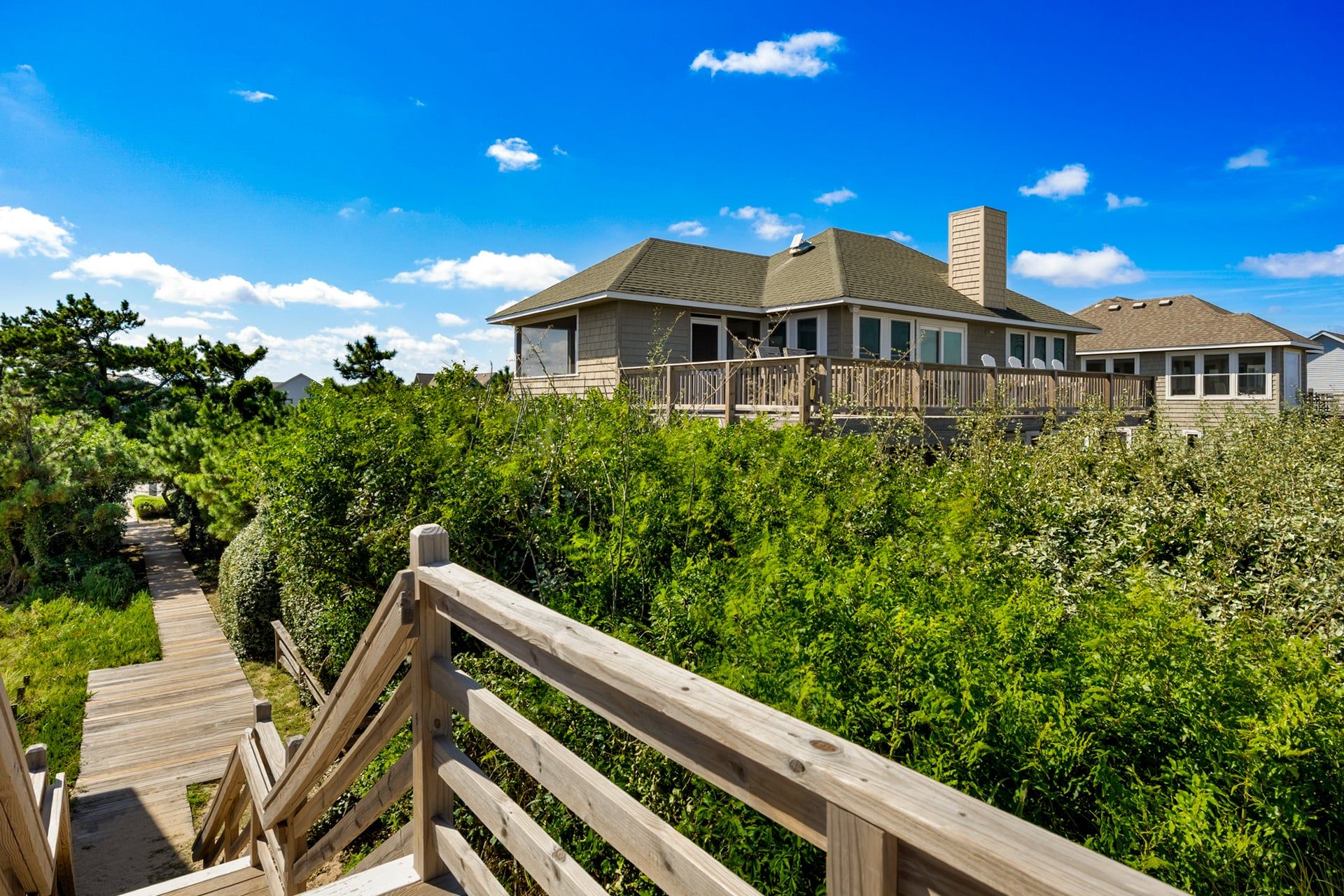 A two-story house with a wooden deck and a pathway leading to it.