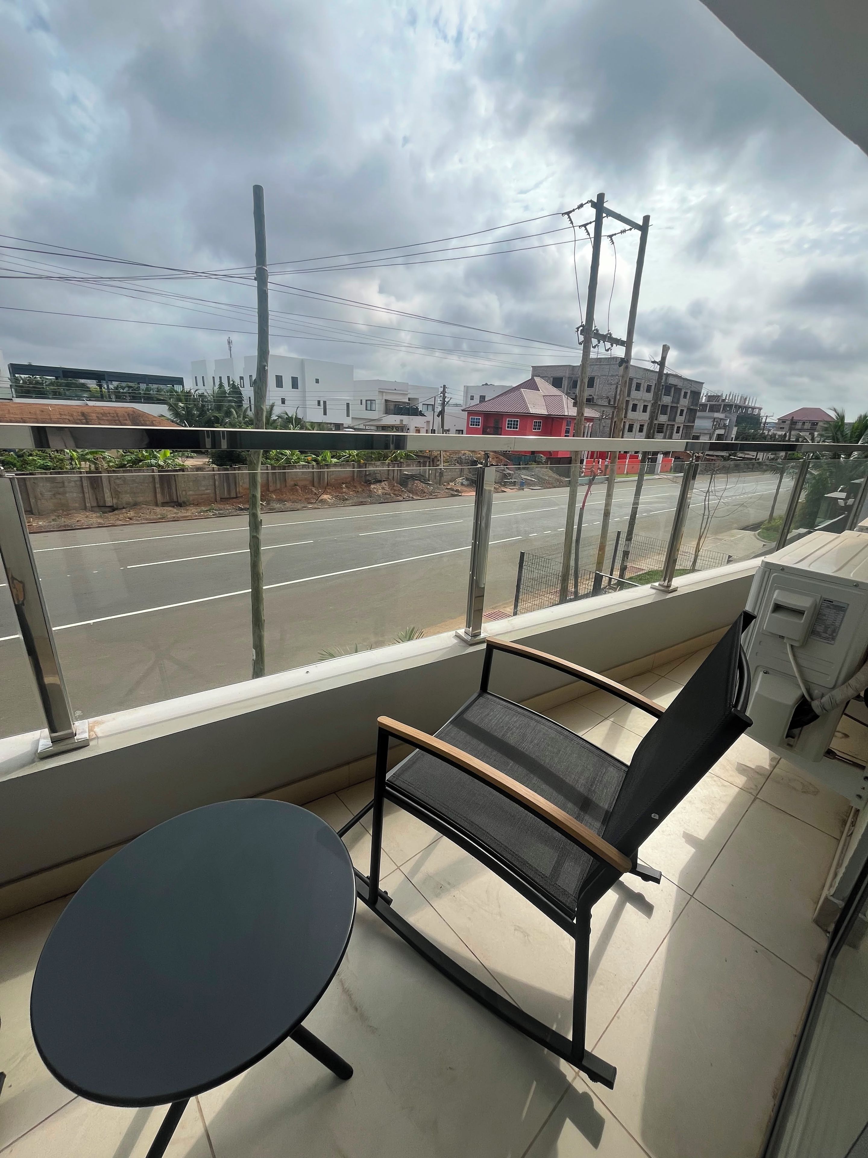 Ein Balkon mit Tisch und Stuhl, mit Blick auf eine Straße, im Hintergrund Gebäude und Bauarbeiten.