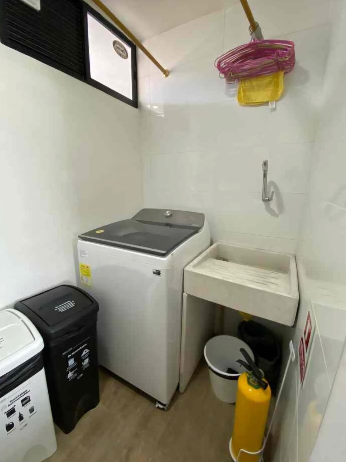 Cocina compacta con lavadora, lavamanos, cubo de basura y extintor.