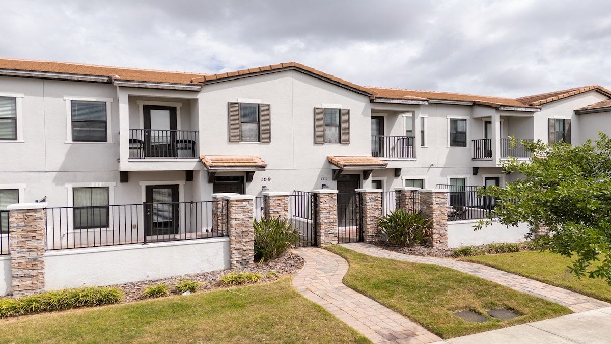 A multi-story residential building with a stone facade, balconies, and a paved walkway.