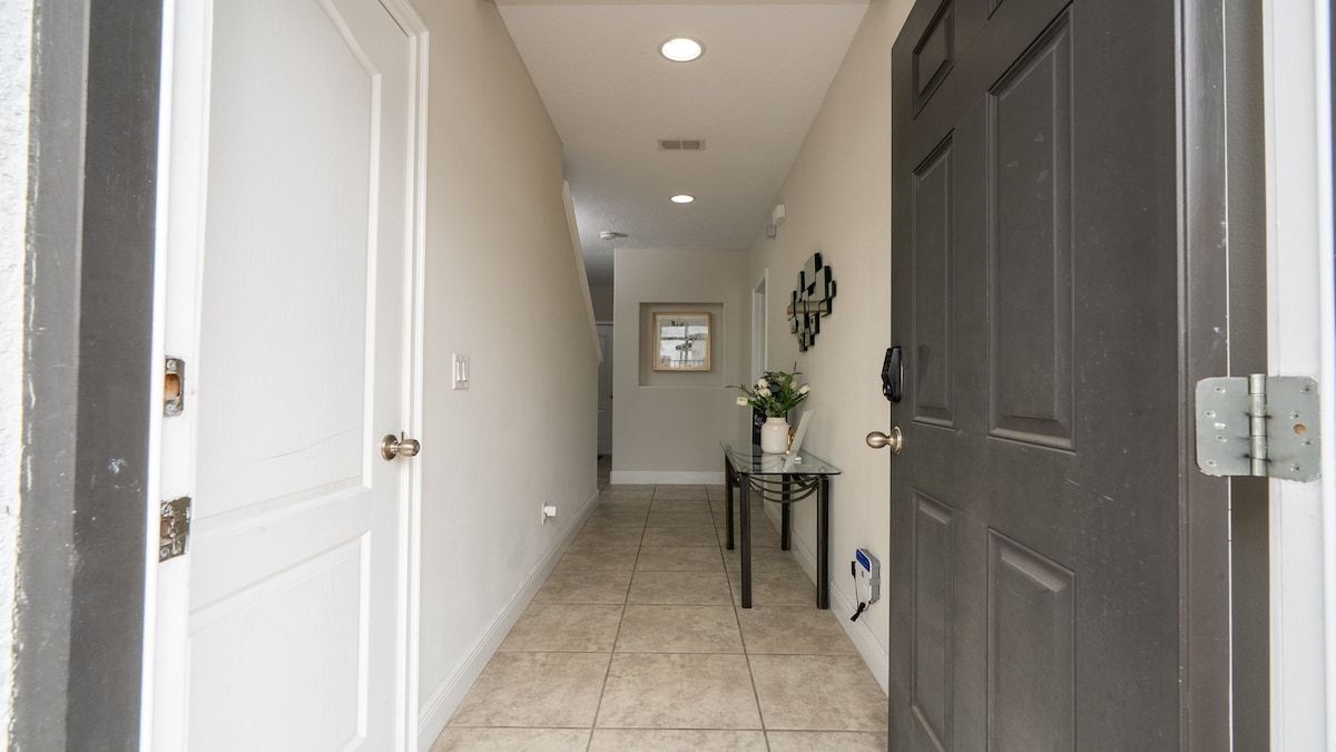 A hallway with a white door on the left, a dark door on the right, and a small table with a vase and flowers in the center.