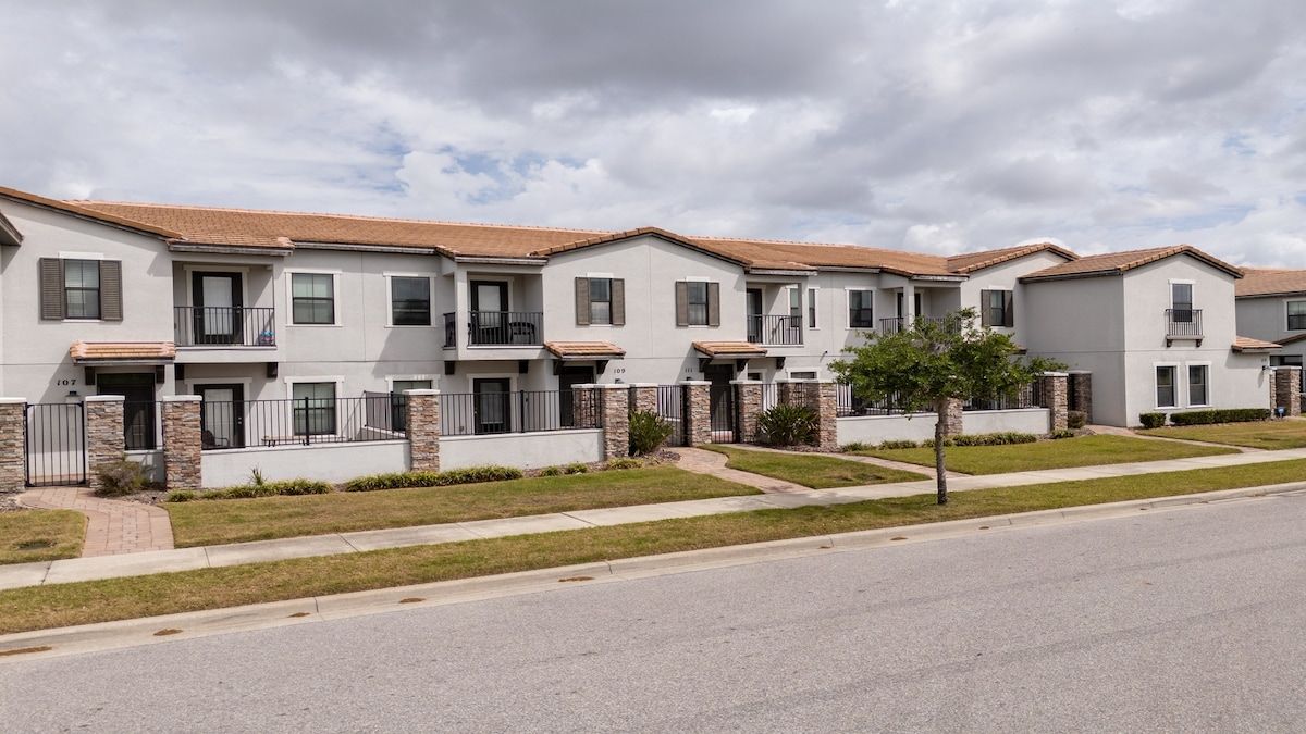 A row of townhouses with balconies, a paved driveway, and a clear sky.