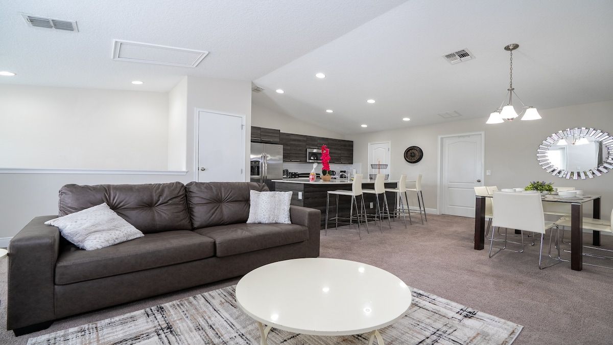 A modern living room with a sofa, a coffee table, and a dining area with chairs and a table.