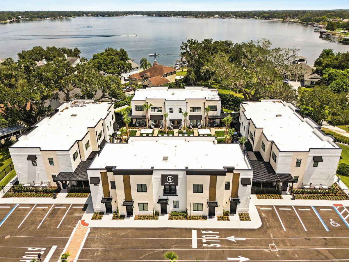 A hotel with a central courtyard, surrounded by parking spaces and a body of water in the background.