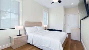 A hotel room with a bed, bedside tables, a ceiling fan, and a TV mounted on the wall.