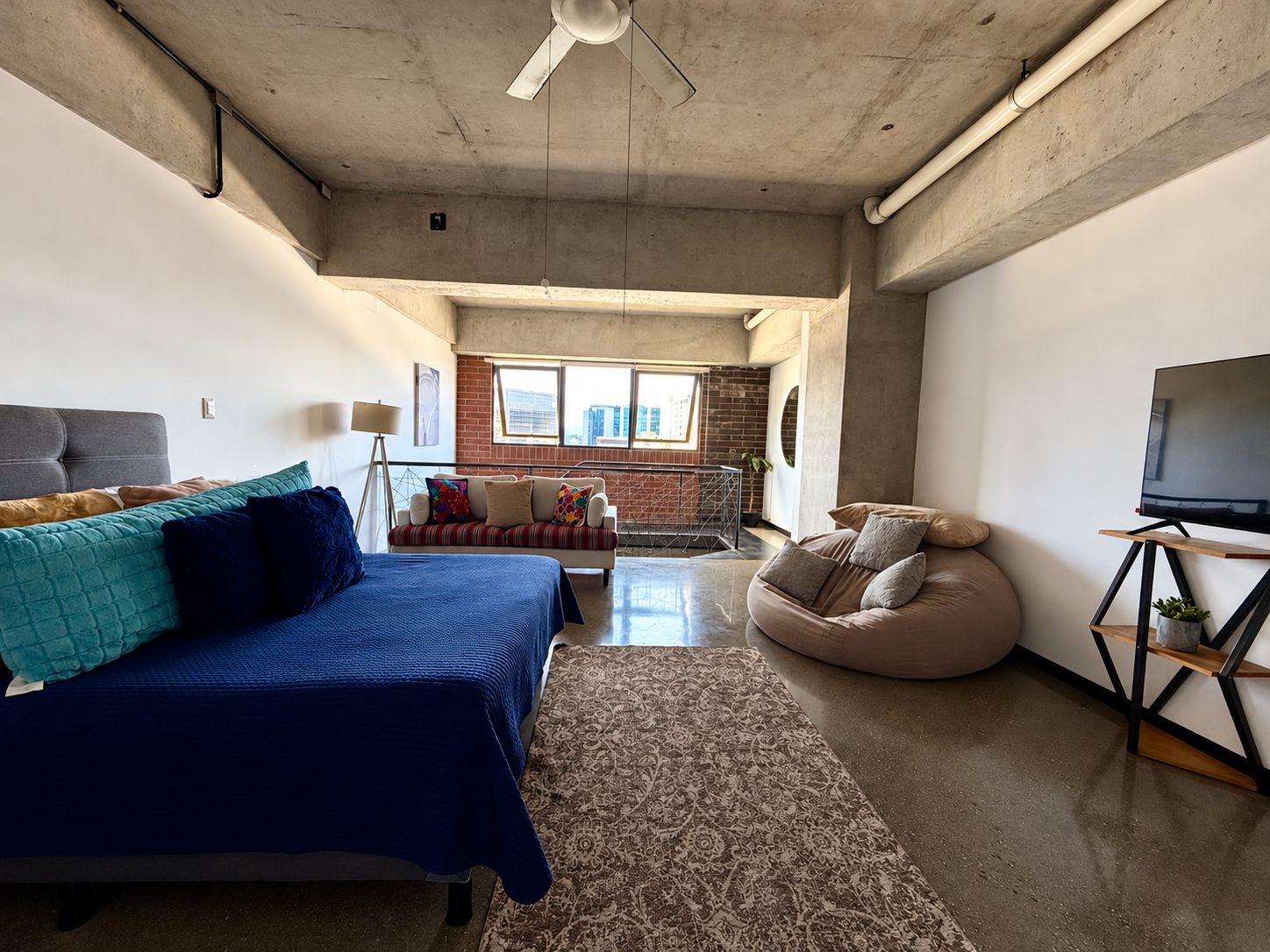 A modern living room with a sofa, a bean bag, a bed, and a TV.