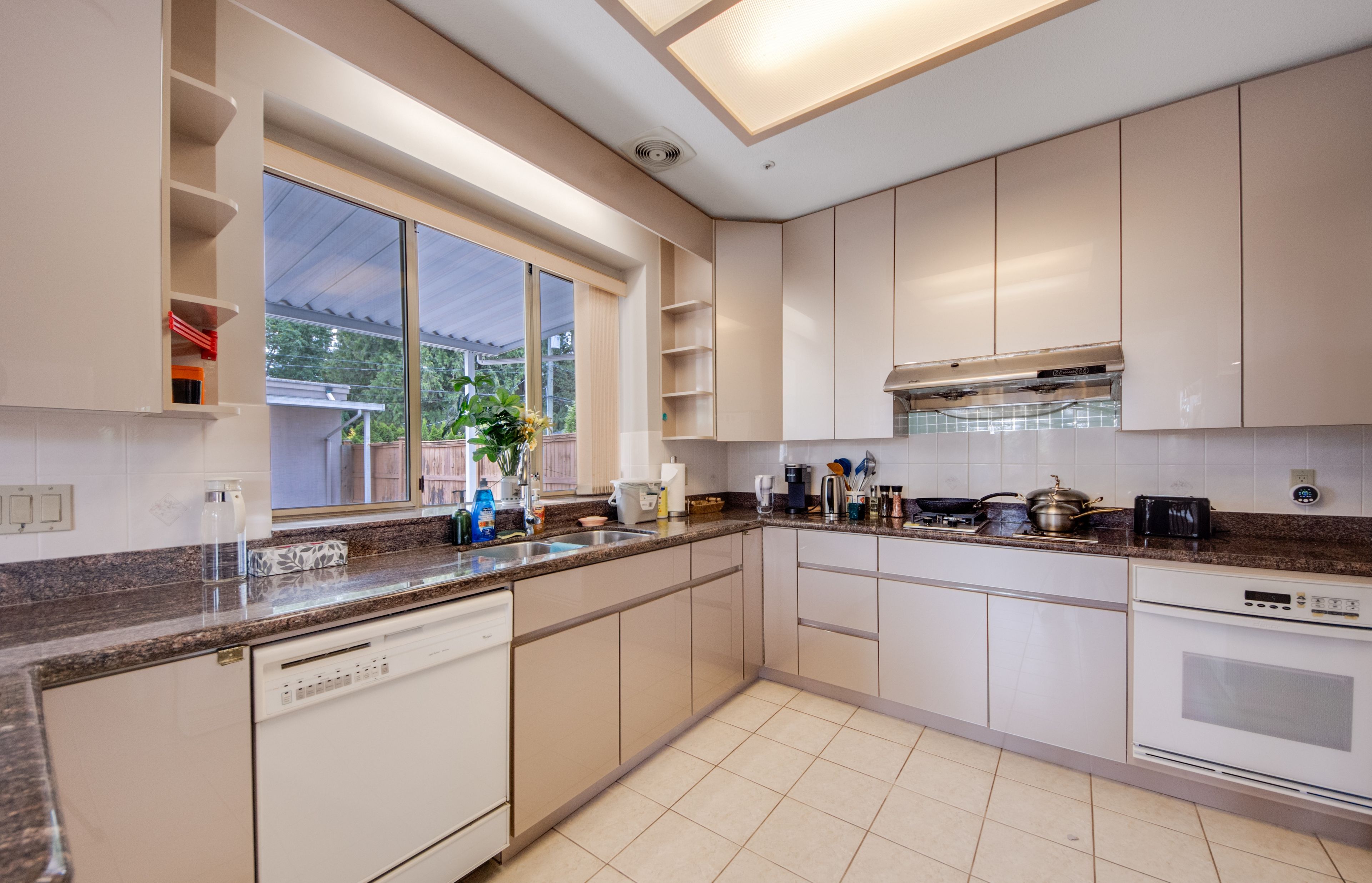 A modern kitchen with a dishwasher, oven, and a large window.