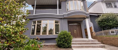 Una casa de dos pisos con un porche cubierto, una puerta principal y un pequeño jardín delantero.