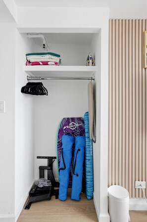 Ein kleiner Stauraum mit Regalen für gefaltete Kleidung, einer Kleiderstange für Taschen und einem Tisch mit Mülleimer.