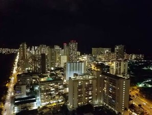 A nighttime cityscape with high-rise buildings, illuminated windows, and a coastline. - [New] Ocean View 2 bedroom 2 bath in Waikiki (Honolulu)