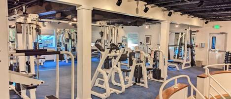 A gym with various exercise machines, a blue carpet floor, and a wooden bench.