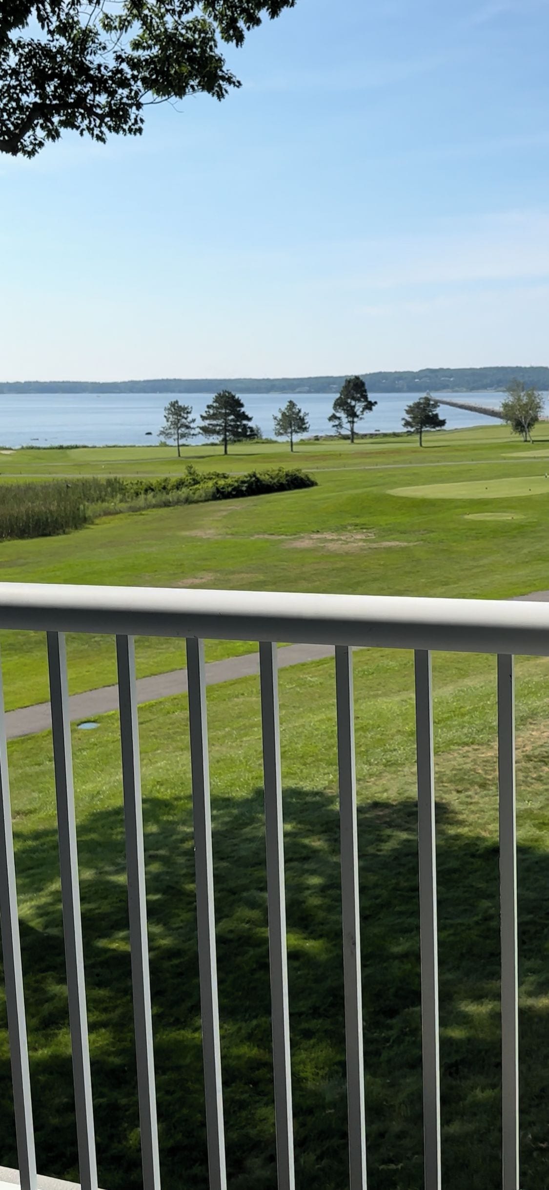 A view from a balcony overlooking a golf course with a body of water in the background.