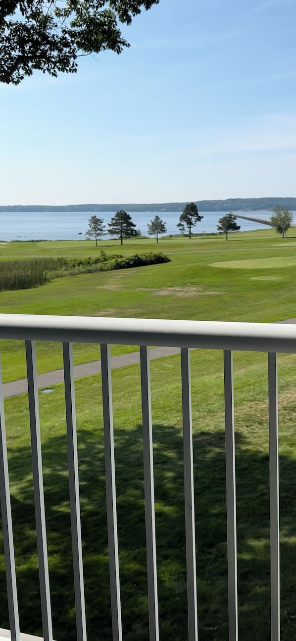 A view from a balcony overlooking a golf course with a body of water in the background.