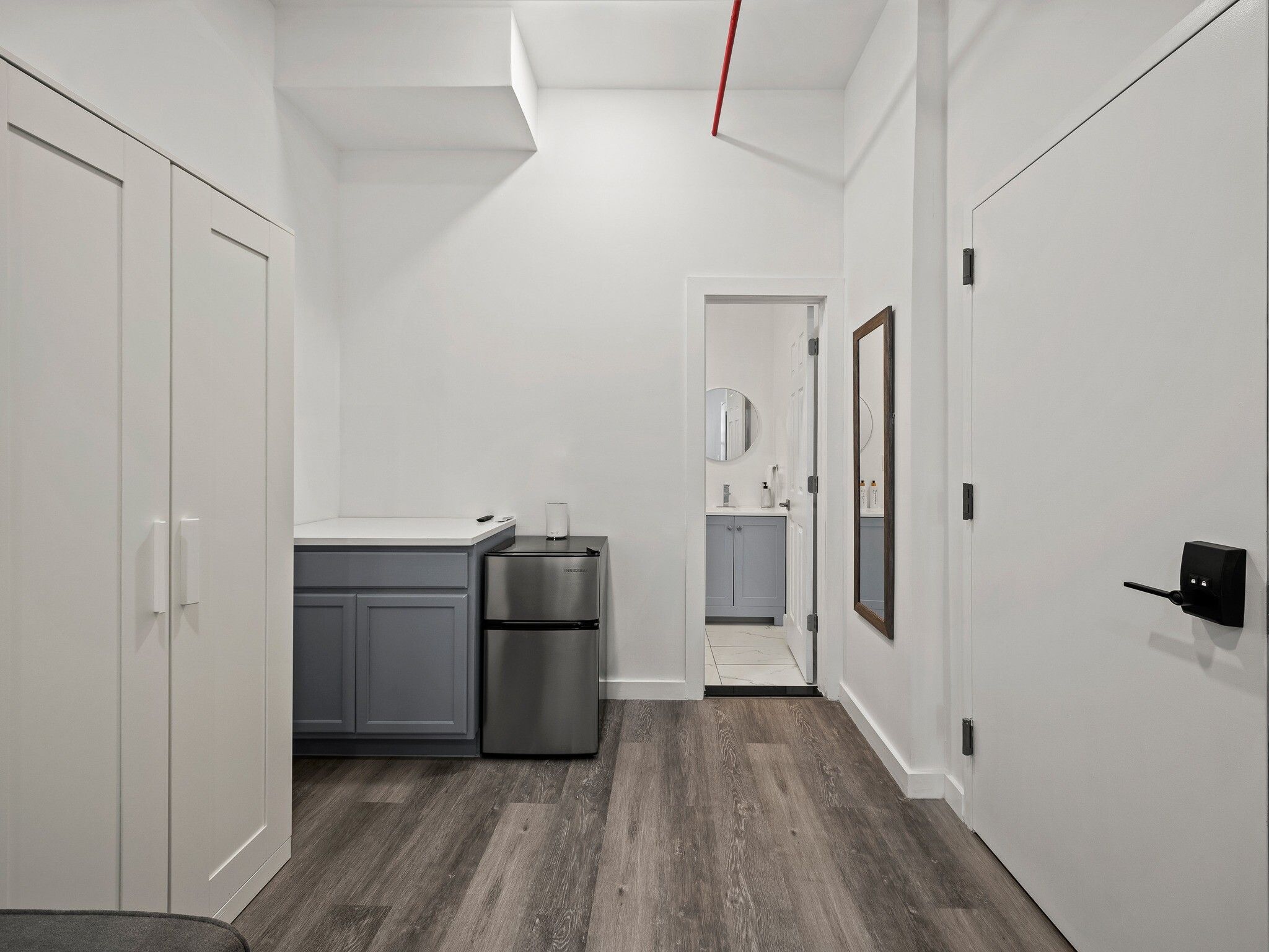 A narrow hallway with a kitchenette area, a refrigerator, and a door leading to a bathroom.