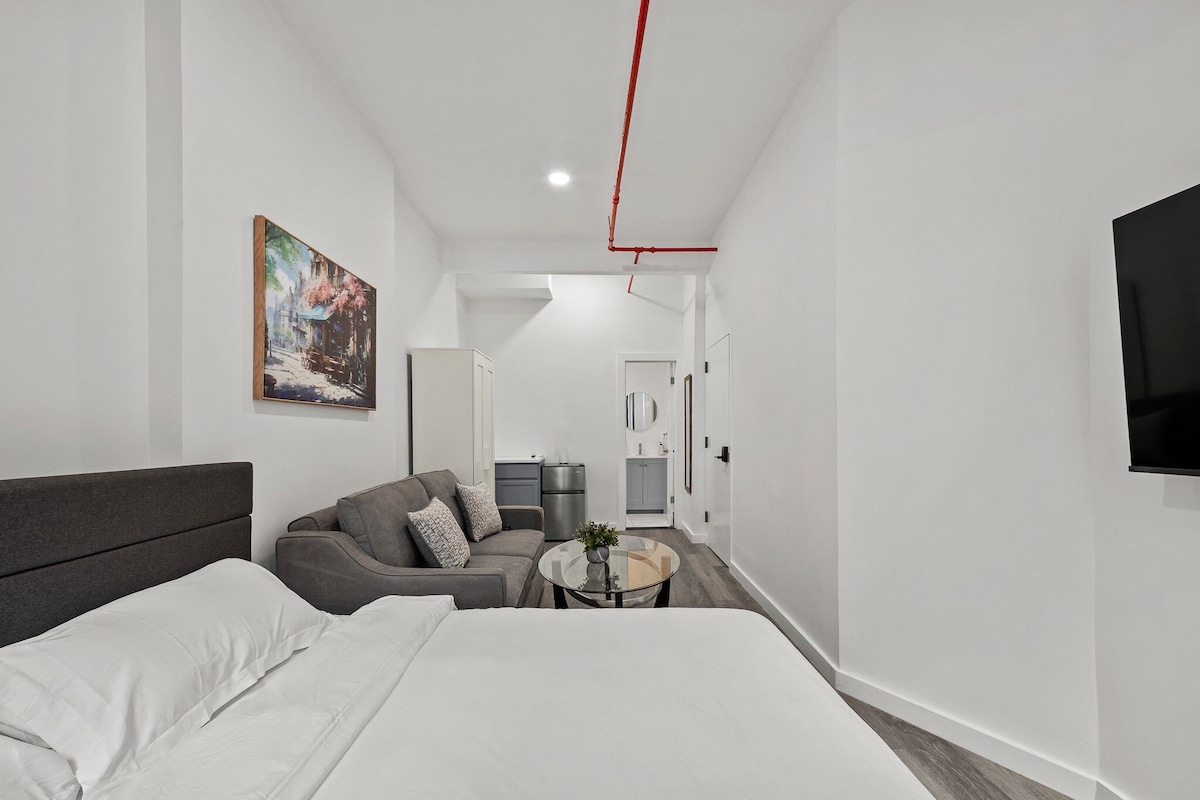A modern hotel room with a large bed, a sofa, a small round table, and a painting on the wall.
