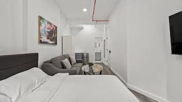A modern hotel room with a large bed, a sofa, a small round table, and a painting on the wall.