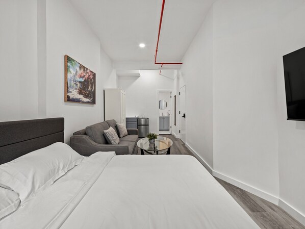 A modern hotel room with a large bed, a sofa, a small round table, and a painting on the wall.