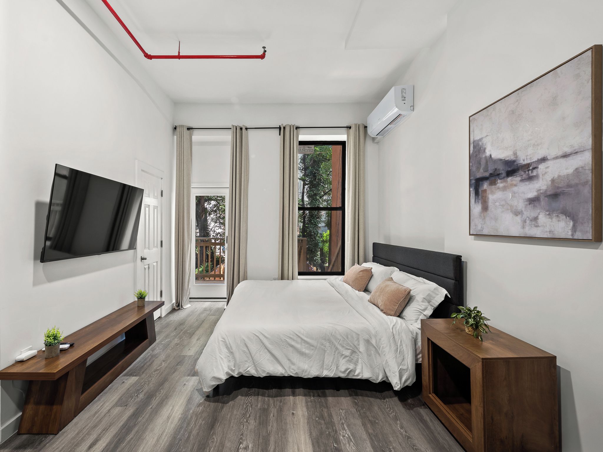 A modern bedroom with a bed, a TV, a painting, and a window with curtains.