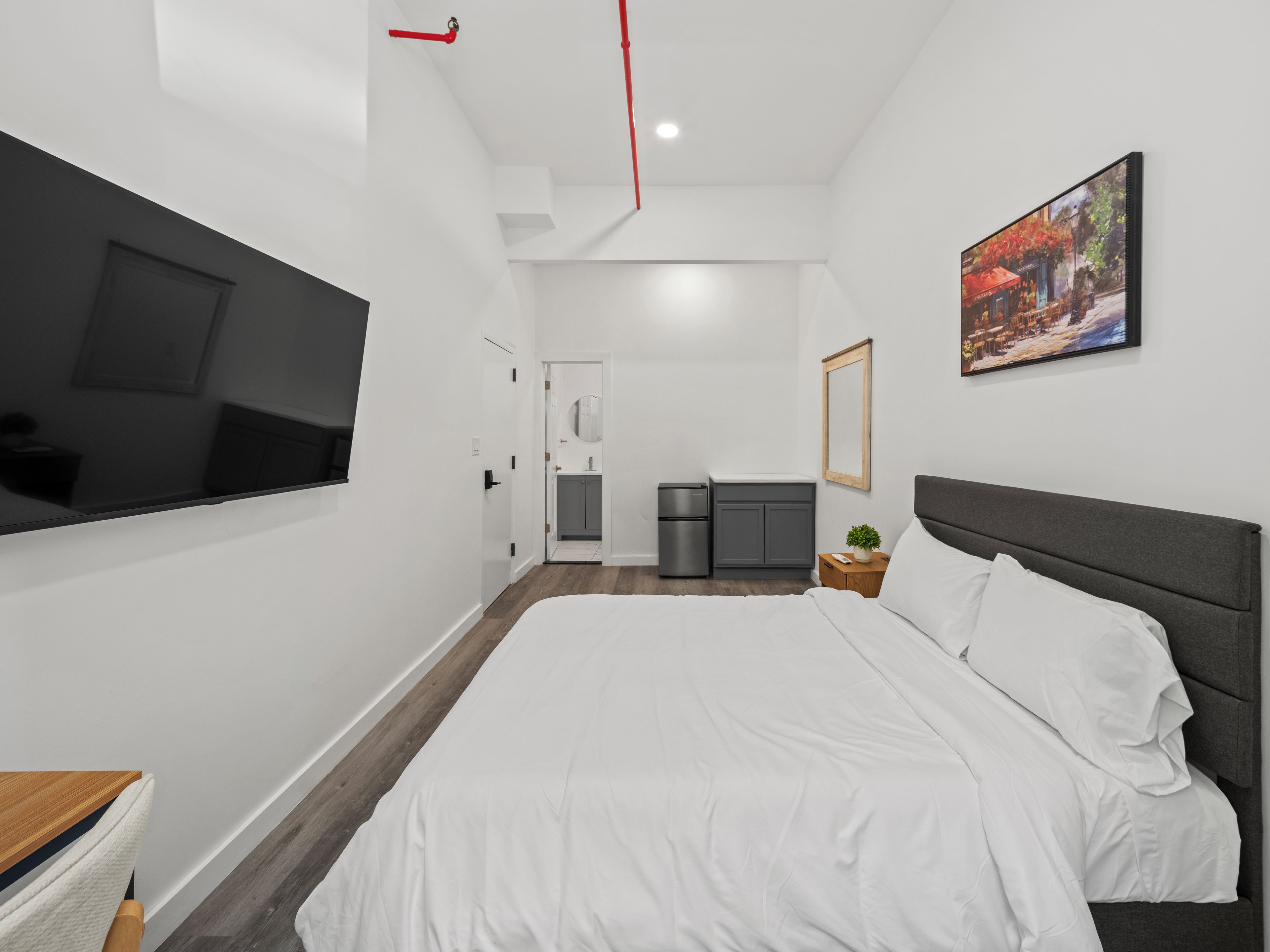 Une chambre d’hôtel moderne dotée d’un grand lit, d’un téléviseur à écran plat fixé au mur, d’une petite kitchenette et d’un tableau décoratif.