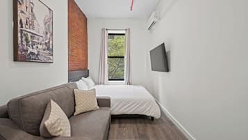 Un dormitorio moderno con una cama, un sofá, un televisor y una ventana con cortinas.