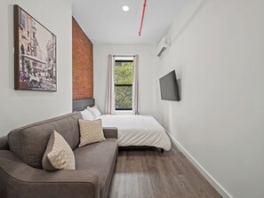 Un dormitorio moderno con una cama, un sofá, un televisor y una ventana con cortinas.
