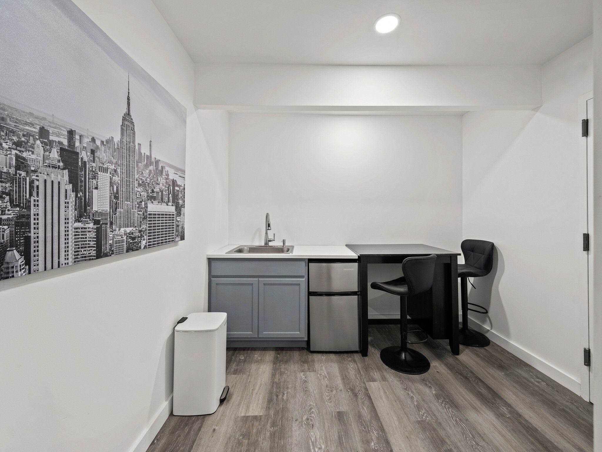 A compact kitchen with a sink, a refrigerator, and a dining area with a chair.