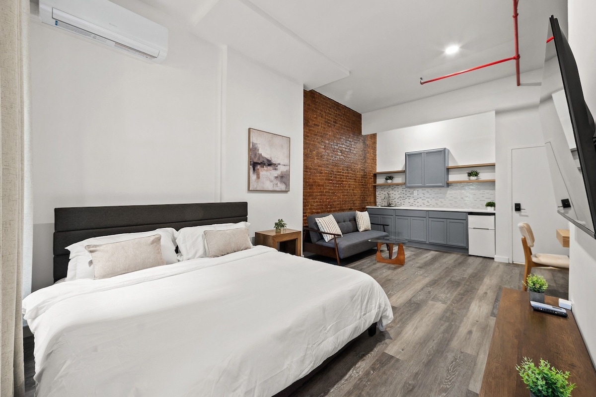 A modern bedroom with a large bed, a grey sofa, and a small table.