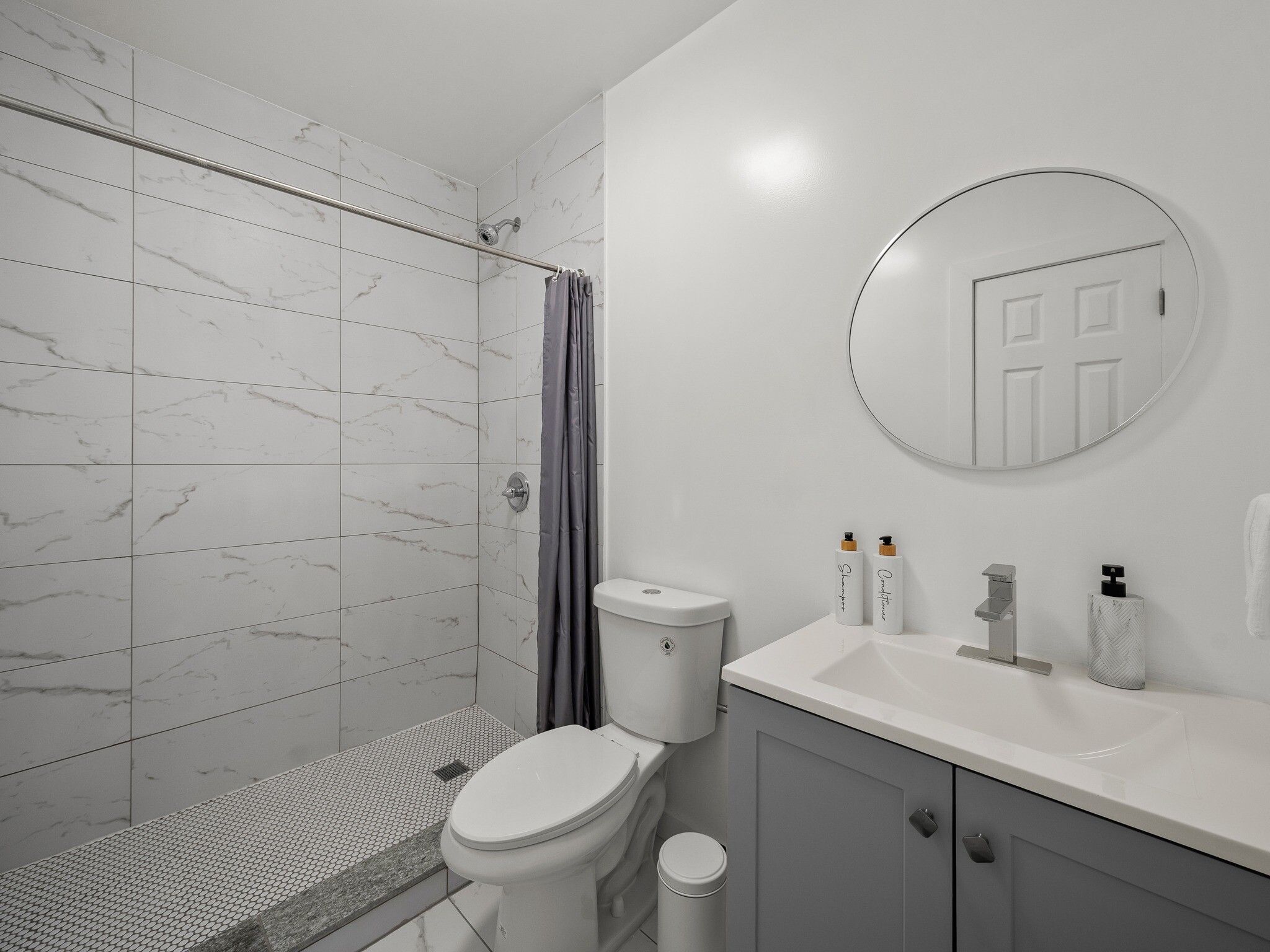 Un baño con ducha, inodoro, lavamanos y un espejo que refleja una puerta.