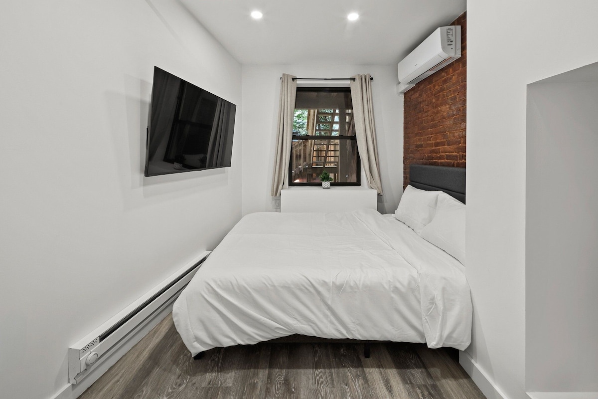 A modern bedroom with a bed, a window with curtains, a wall-mounted TV, and a red ceiling light fixture.