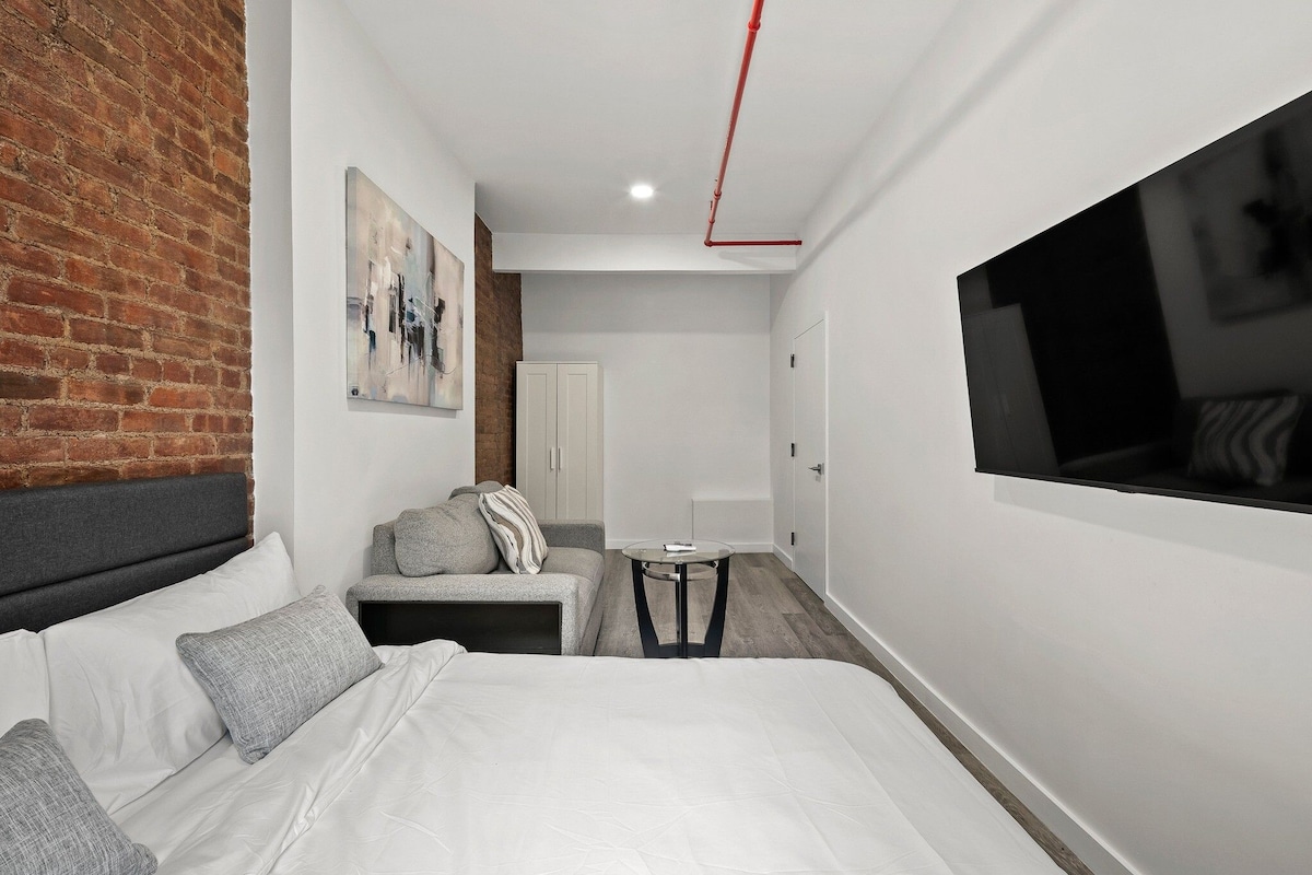 A modern hotel room with a large bed, a seating area with a table, and a TV mounted on the wall.