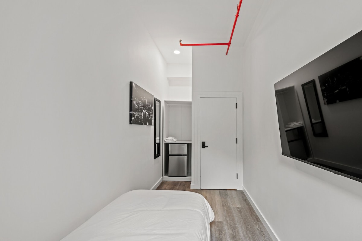 A narrow hallway with a bed, a door, and a small kitchenette.