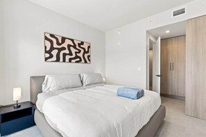 Ein Schlafzimmer mit einem Bett, einem Nachttisch, einem an der Wand befestigten abstrakten Kunstwerk und einem Kleiderschrank.